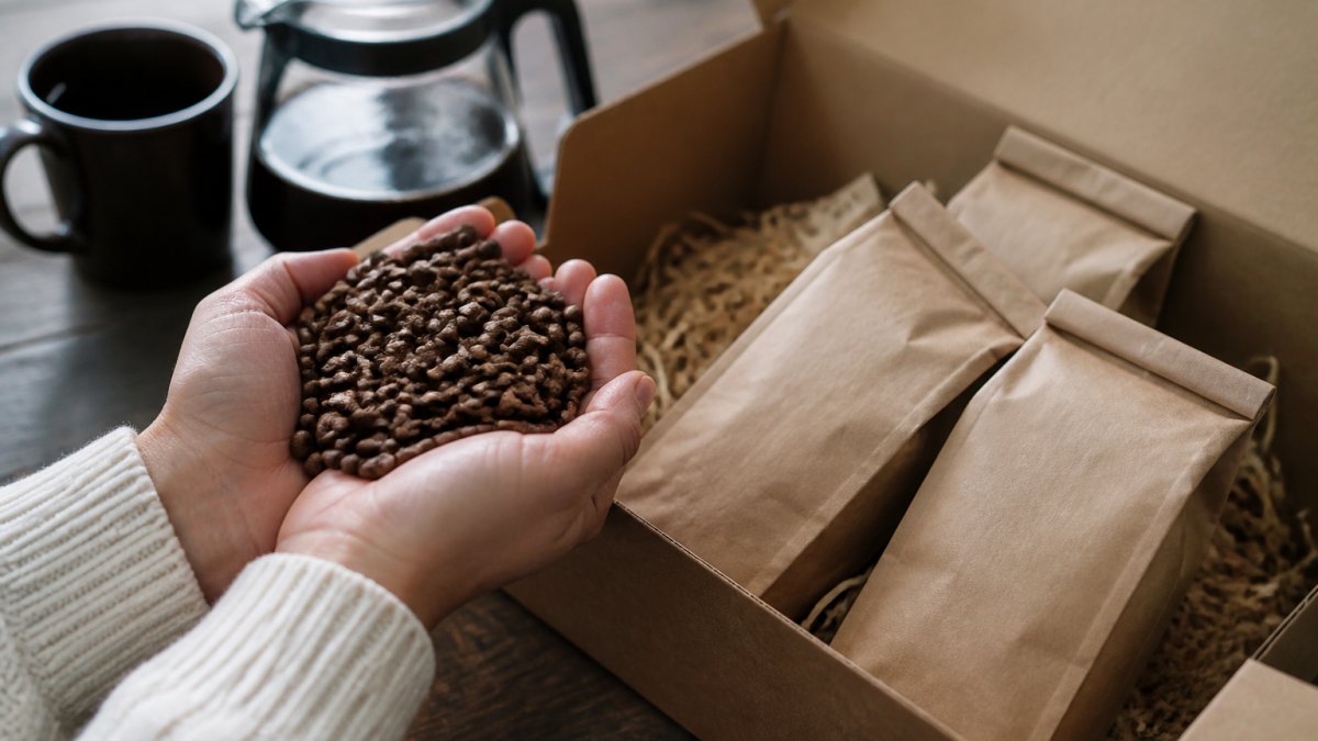 Close-up of hands holding freshly roasted whole coffee beans over a wooden table with a coffee subscription box open nearby