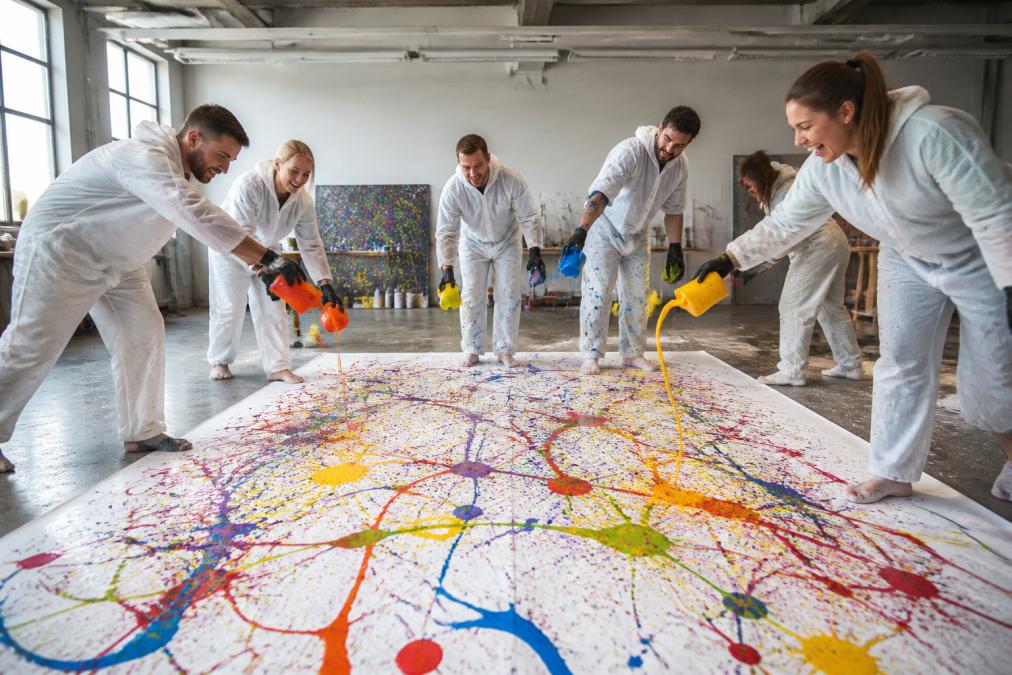 Eine Gruppe von Menschen in weißen Schutzanzügen beim Action Painting Workshop, bunte Farben spritzend und fließend auf eine große weiße Leinwand, konzentrierte und lachende Gesichtsausdrücke, moderner heller Raum mit professioneller Beleuchtung