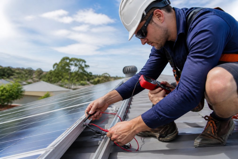 Qualified solar technician connecting monocrystalline panel wiring during residential installation, checking voltage readings with multimeter, showing professional workmanship and safety protocols in action