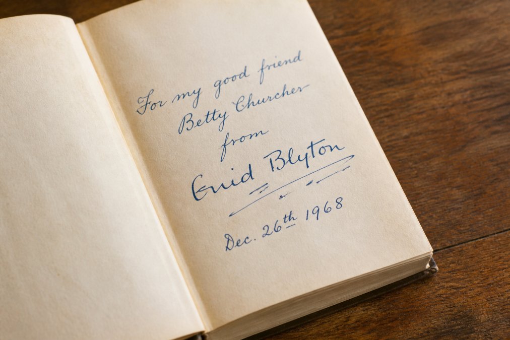 Close-up of an open vintage book showing a hand-signed inscription on the title page, with natural lighting highlighting ink flow and penmanship details