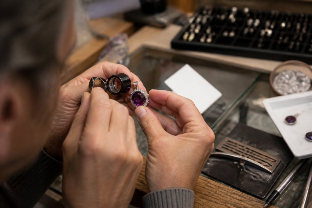 Jeweler examining a gemstone jewelry pendant with a loupe next to a certification card on a shop counter