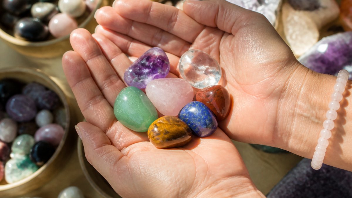 Close-up of hands holding authentic tumbled crystals with natural light showing color depth, surface texture, and clarity details