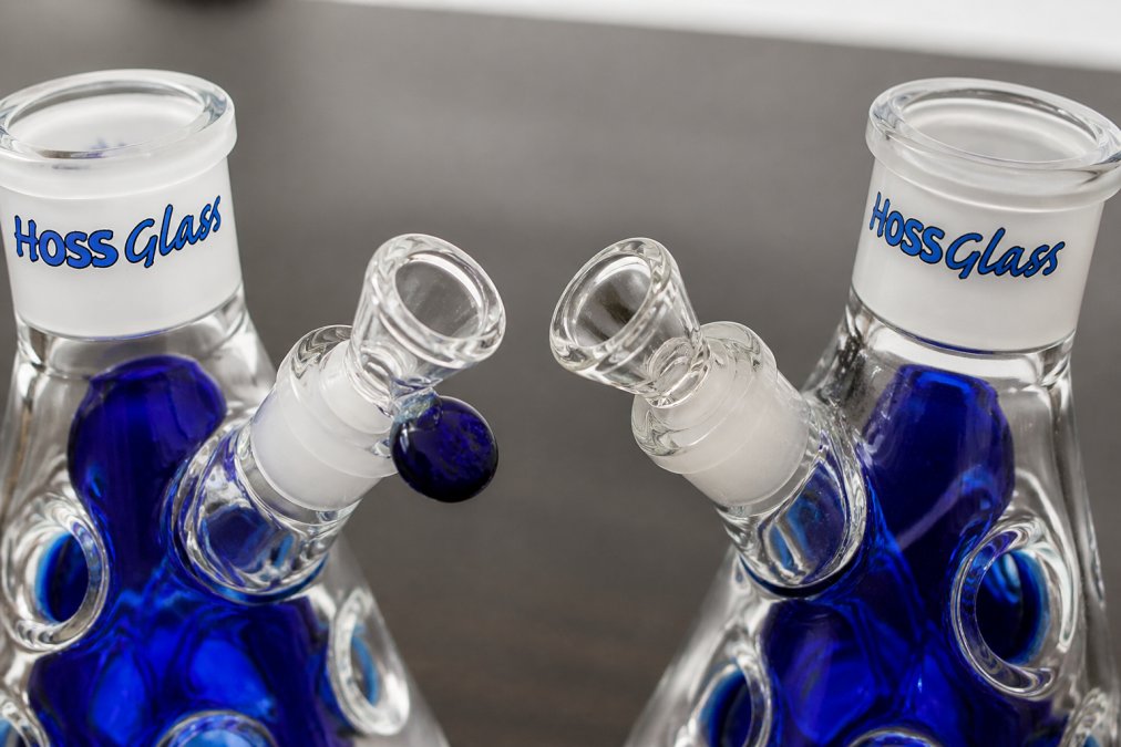 Close-up macro photography of authentic glass bong joint showing crisp, perfectly aligned 19mm female joint connection with smooth edges and uniform wall thickness, contrasted with counterfeit piece displaying uneven joint edges, misaligned connection point, and visible stress marks