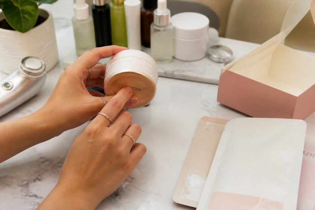 Close-up of hands inspecting Korean skincare product bottle, examining batch code printed on bottom, reading label details and packaging information under bright lighting