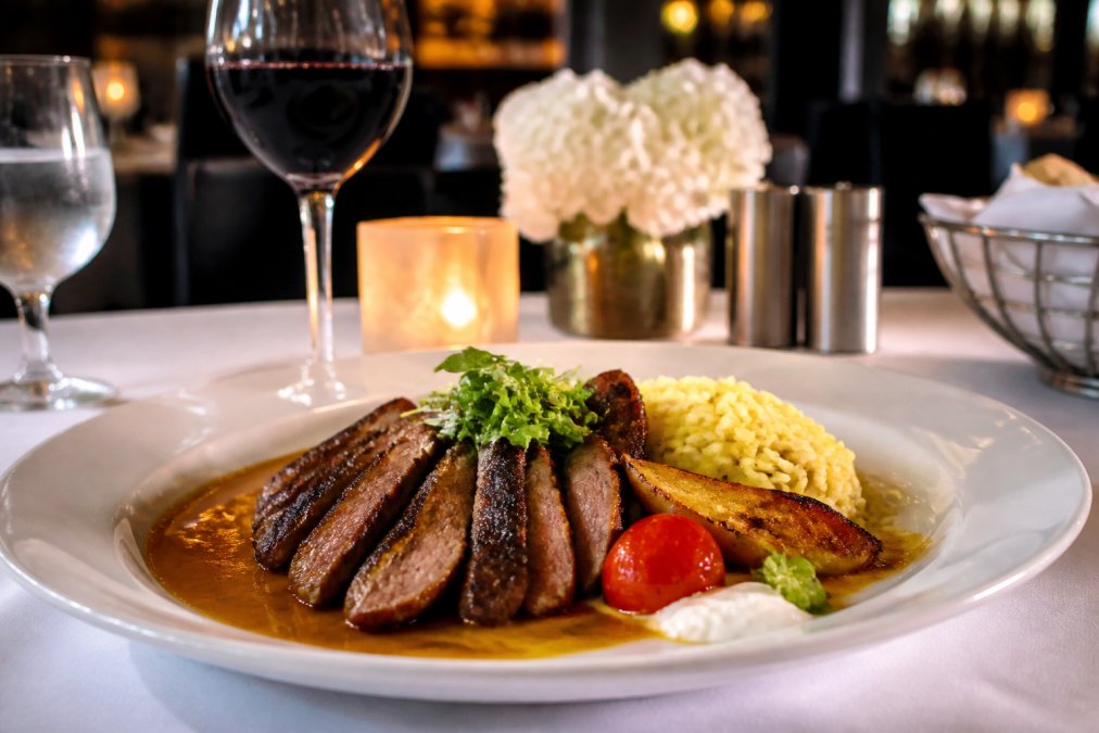 Elegantly plated Mediterranean entrée on a white ceramic plate at an upscale restaurant table, with soft ambient lighting, wine glasses, and warm candle glow in the background