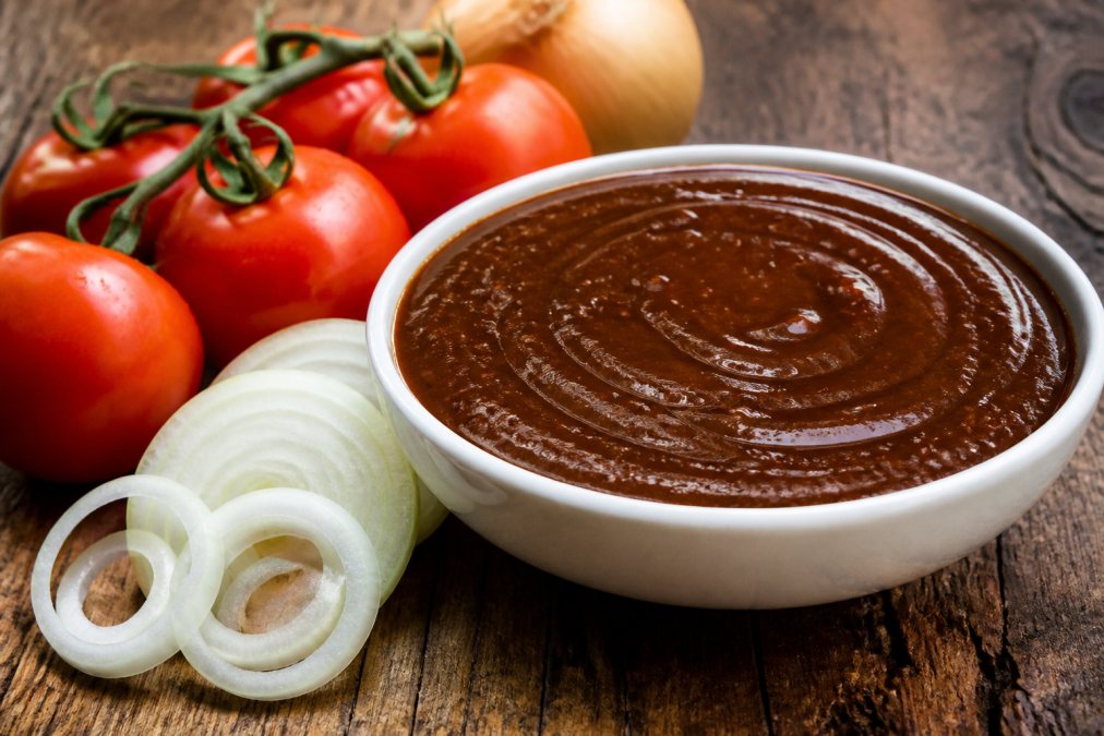 Glossy Monkey Gland sauce in a white bowl with fresh tomatoes and onions for southern African sauce recipes