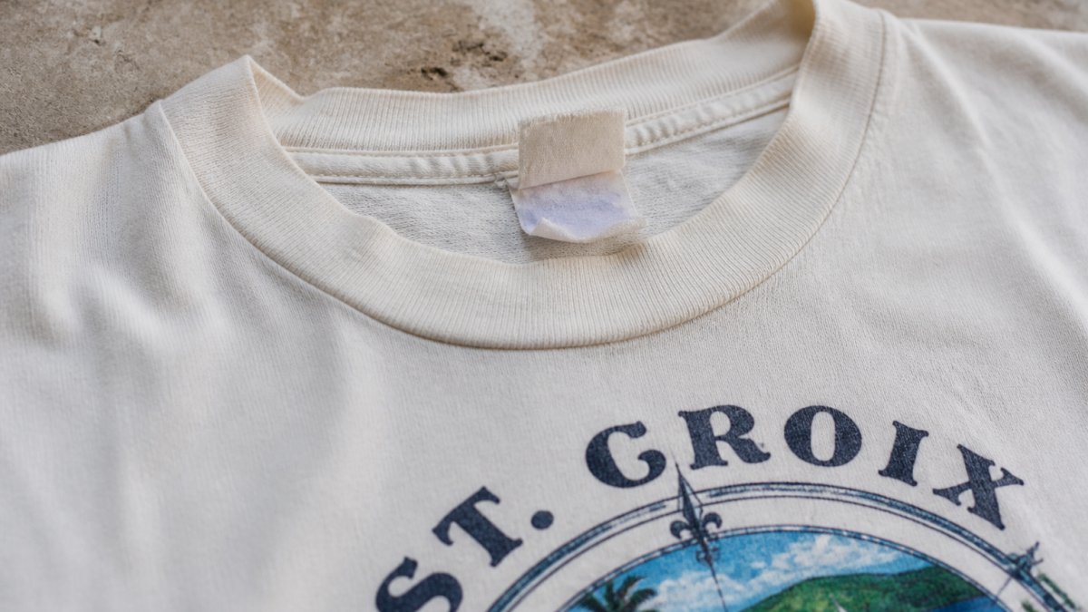Close-up of vintage St Croix graphic T-shirt showing tag details, label stitching, and fabric texture laid flat on neutral surface with natural lighting