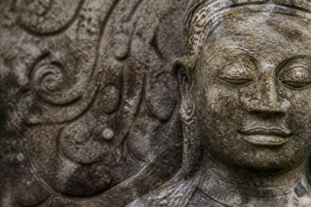 Close-up of aged stone Buddha statue surface showing natural patina, weathering patterns, and hand-carved texture with visible aging marks and mineral deposits