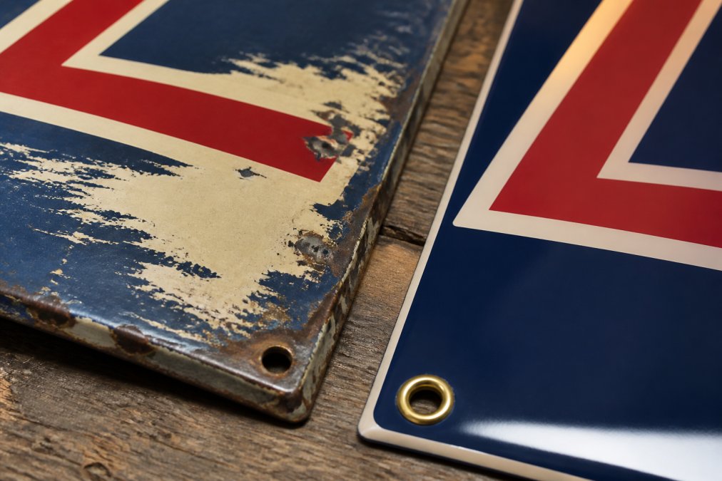 Close-up of authentic vintage metal signage showing original paint patina, hand-stamped edges, and brass hardware details alongside a modern reproduction piece, demonstrating craftsmanship differences under natural studio lighting