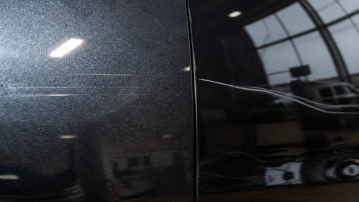 Close-up van autolak met verschillende soorten krassen zichtbaar - oppervlakkige krassen in de blanke lak en diepere beschadigingen in de kleurlak, professionele werkplaats verlichting