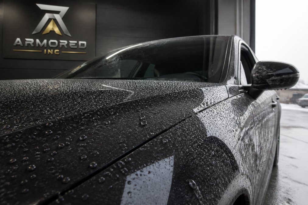 Close-up of vehicle paint surface showing water beading and hydrophobic properties after ceramic coating application, with winter road salt and moisture visible on surrounding surfaces