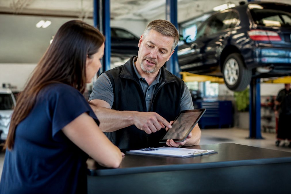 Service advisor explains auto repair financing options to a customer on a tablet at a modern mechanic shop.