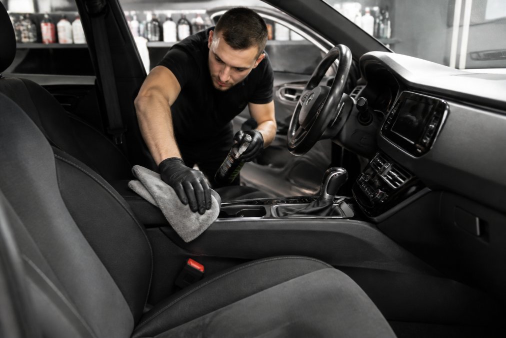 Persoon die het interieur van een auto schoonmaakt met speciale interieur reinigingsmiddel en microvezeldoeken, stoelen en dashboard zichtbaar
