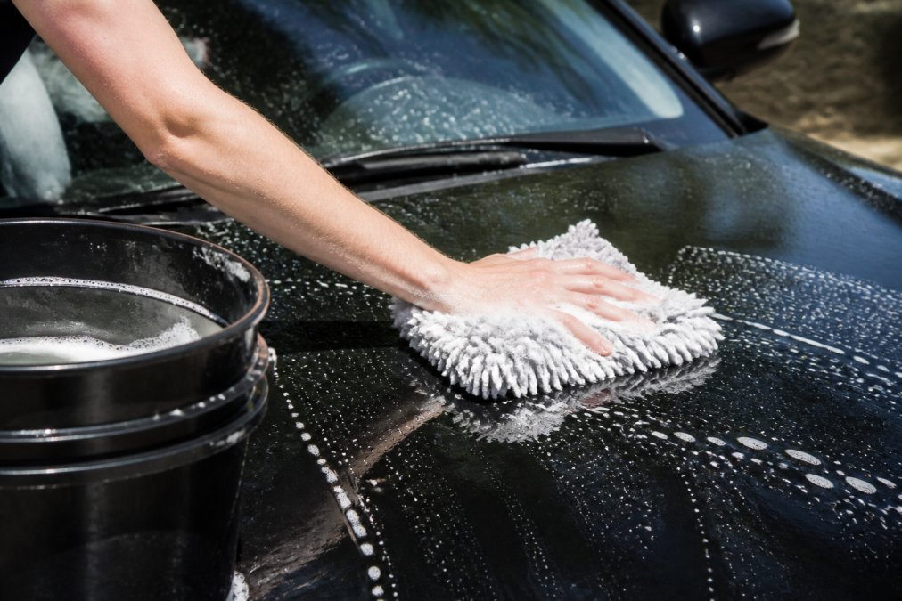 Close-up van handen die een auto wassen met een zacht microvezelspons en warm water, waarbij de juiste wassponge-techniek wordt getoond in daglicht