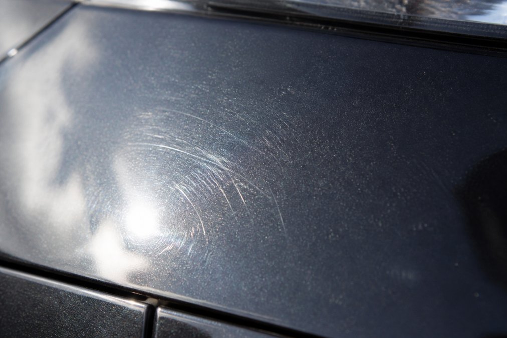 Detail van een auto's lakoppervlak met zichtbare lichte krassen en oneffenheden, onder helder daglicht waarbij de textuur duidelijk zichtbaar is