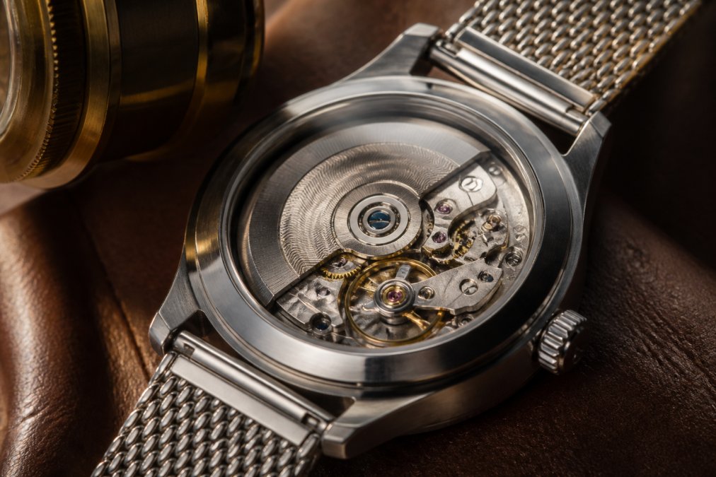 Extreme close-up of an open caseback watch revealing a decorated automatic movement with a spinning rotor, visible balance wheel, and jewel bearings under warm amber studio lighting