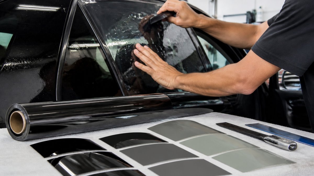 Professional installer using a squeegee for precise window tinting customization on a car side window