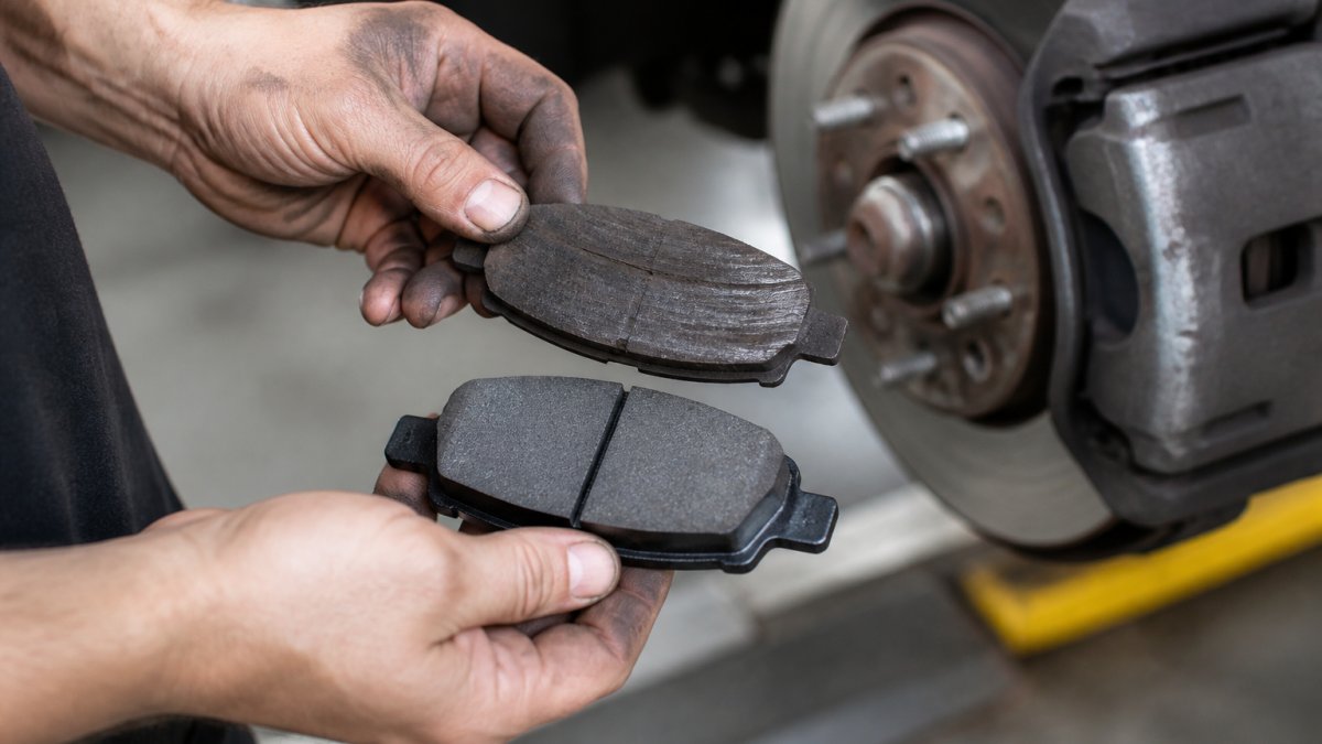 Close-up of a worn brake pad next to a new one, showing thickness difference and dark wear patterns on the friction material surface