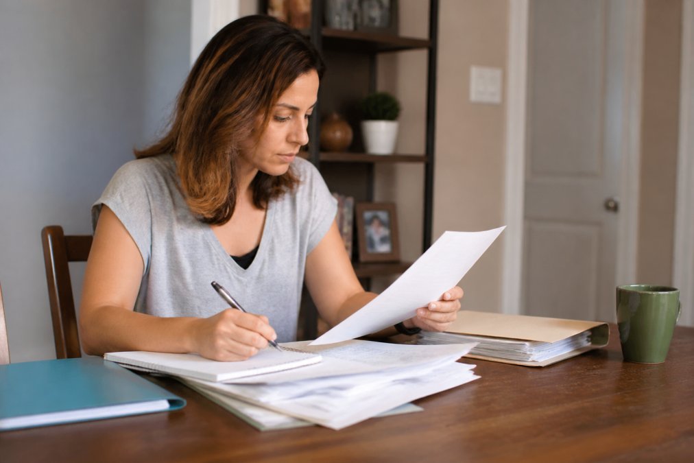 Patient reviewing healthcare insurance documents and cost information at desk with pen and notepad, organized medical paperwork visible