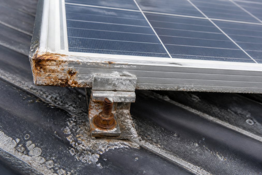 Close-up of corroded solar panel frame and mounting hardware showing rust and salt deposits on coastal residential roof installation