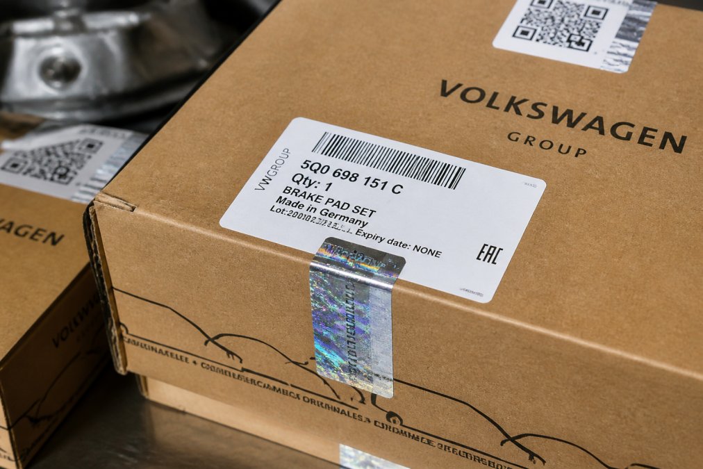 Close-up of genuine OEM automotive part packaging showing crisp, sharp print quality with holographic security features, clear part number labeling, and tamper-evident seals under bright workshop lighting