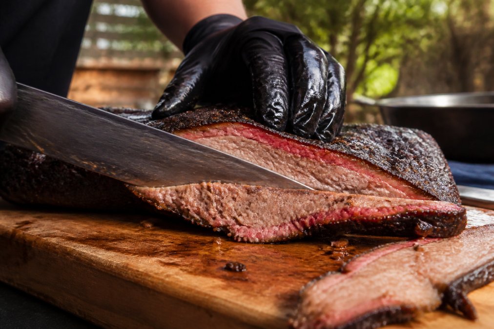 A thick, moist slice of brisket being cut on a wooden board to avoid dry brisket with a visible smoke ring.