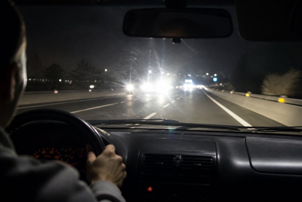 Driver at night on a multi-lane highway with oncoming vehicle headlights visible ahead, demonstrating proper eye positioning and gaze directed toward the right road edge rather than directly at the lights