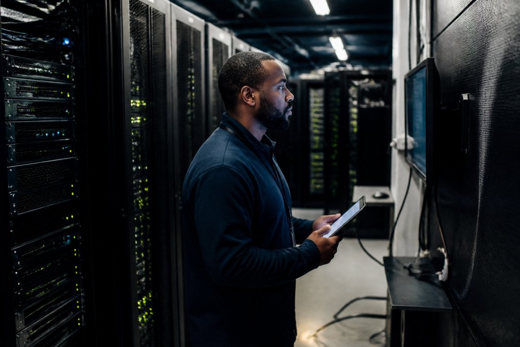 Technician monitoring performance dashboards for dedicated servers in a data center aisle.