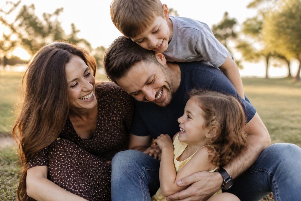 A happy family laughing in a sunlit park with natural movement to avoid stiff poses in portraits