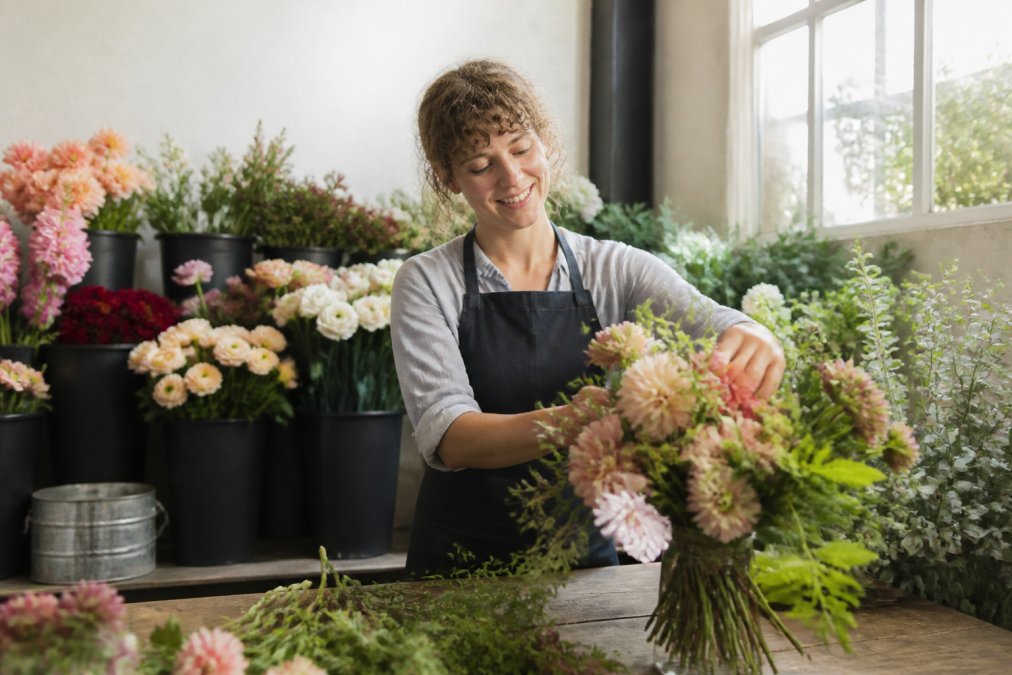 A florist arranging fresh-cut local flowers in a sunlit studio, with buckets of colorful blooms in the background