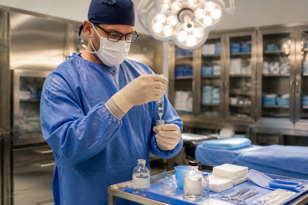 Surgeon preparing local anesthetic for an awake breast augmentation procedure in a modern surgical suite.