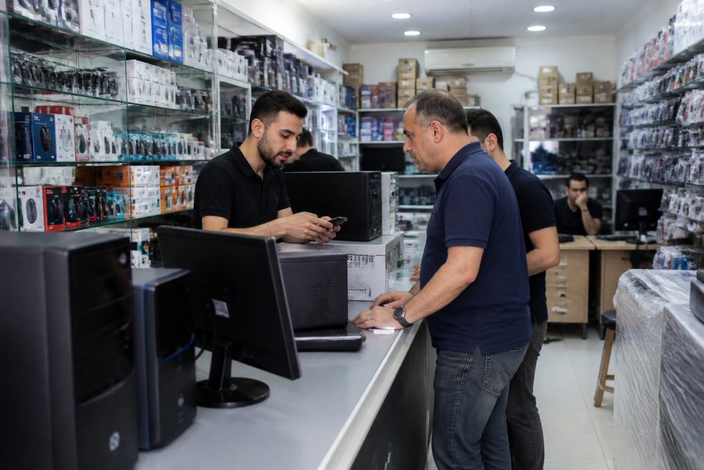 A busy computer retail shop in Lebanon with shelves of hardware, printers, and accessories, staff assisting customers at the counter