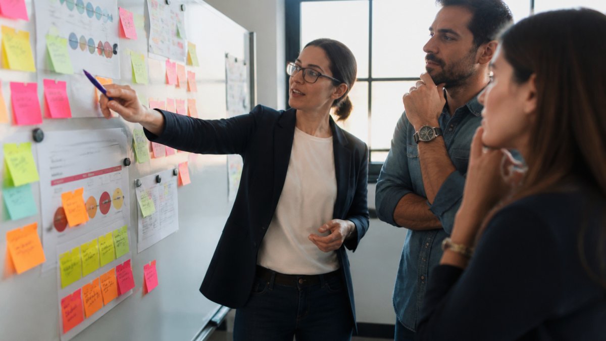 A marketing and sales team collaborating around a whiteboard covered with buyer journey maps and sticky notes in a bright modern office