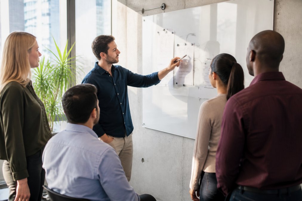 Sales team using a whiteboard to plan B2B lead gen outreach strategies in a bright, modern office space with natural light.