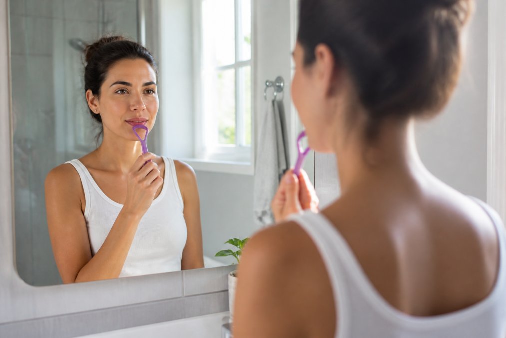Person using a tongue scraper in a bright bathroom to help prevent common bad breath causes