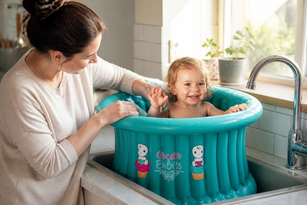Une mère utilise une baignoire bébé durable et compacte dans son évier pour baigner son enfant avec une posture confortable.