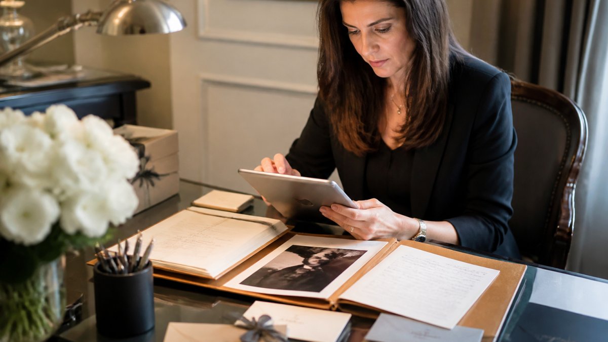 Luxury brand manager reviewing customer data on tablet at elegant desk with personalised client files and handwritten notes nearby