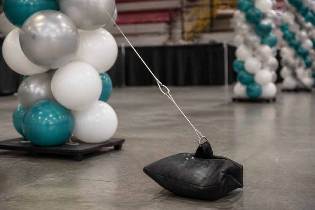 Close-up of weighted base system securing a tall balloon column, showing monofilament line rigging and structural support setup for stability
