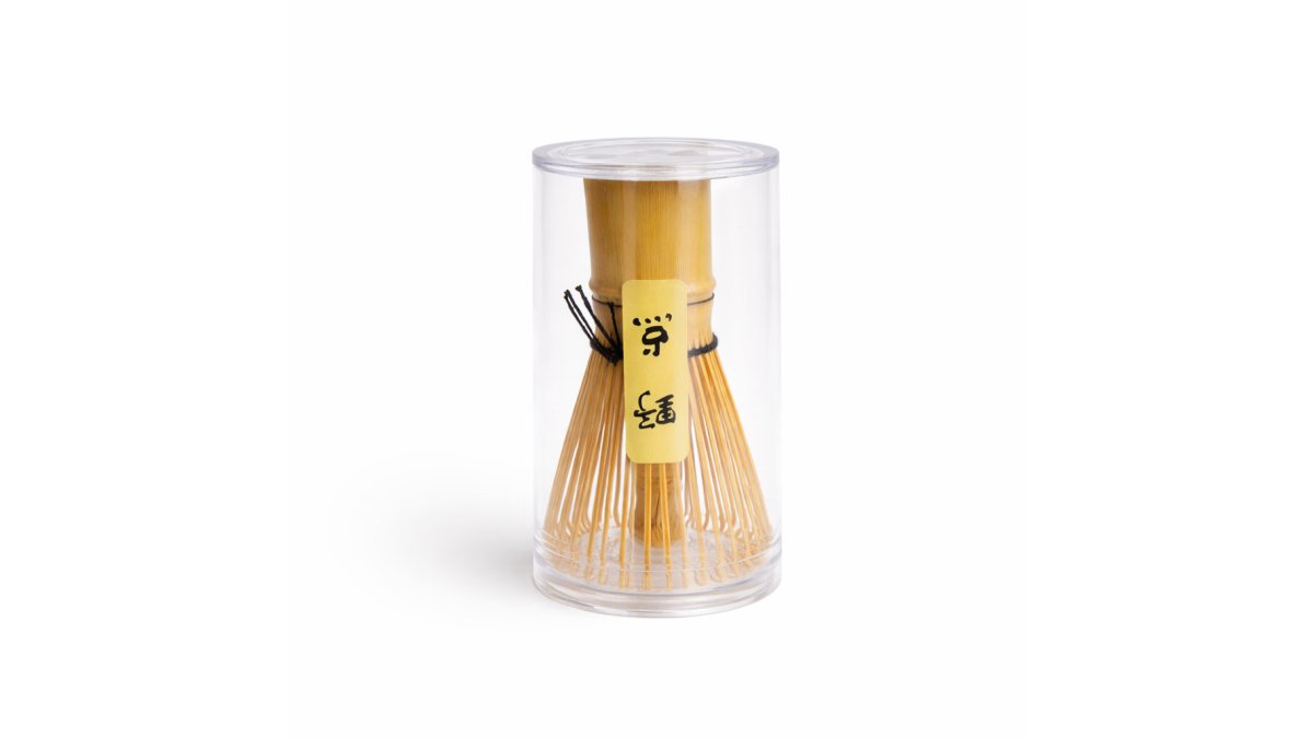 A serene close-up of hands whisking vibrant green matcha in a ceramic bowl on a wooden kitchen bench, with a bamboo whisk and soft morning light filtering through a window, creating a calm, intentional atmosphere