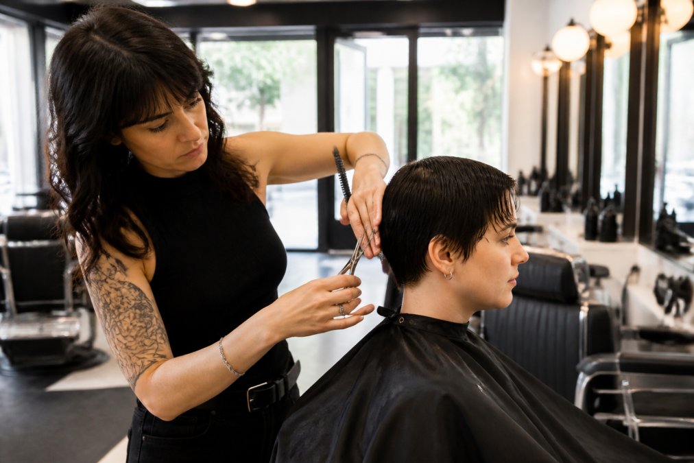 Une barbière professionnelle réalise une coupe courte femme barbier précise avec des ciseaux dans un salon moderne.