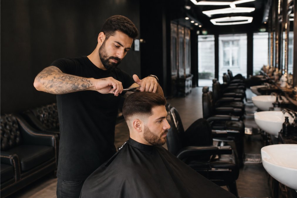 Barbier en train de réaliser une coupe aux ciseaux de précision sur un client dans un salon moderne avec éclairage hexagonal et chaises de cuir