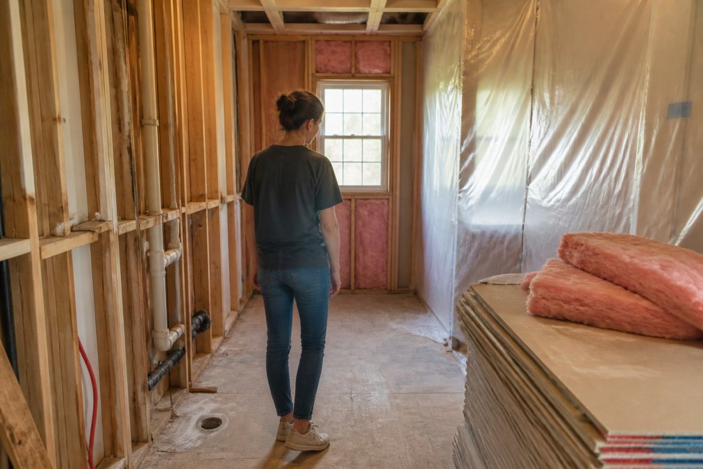 Homeowner navigating a bathroom remodel timeline amidst exposed plumbing and construction debris.