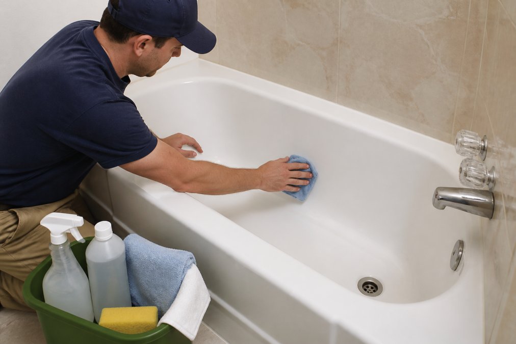 Homeowner carefully cleaning a refinished bathtub using a soft microfiber cloth and mild cleaning solution, demonstrating proper maintenance technique with gentle circular motions