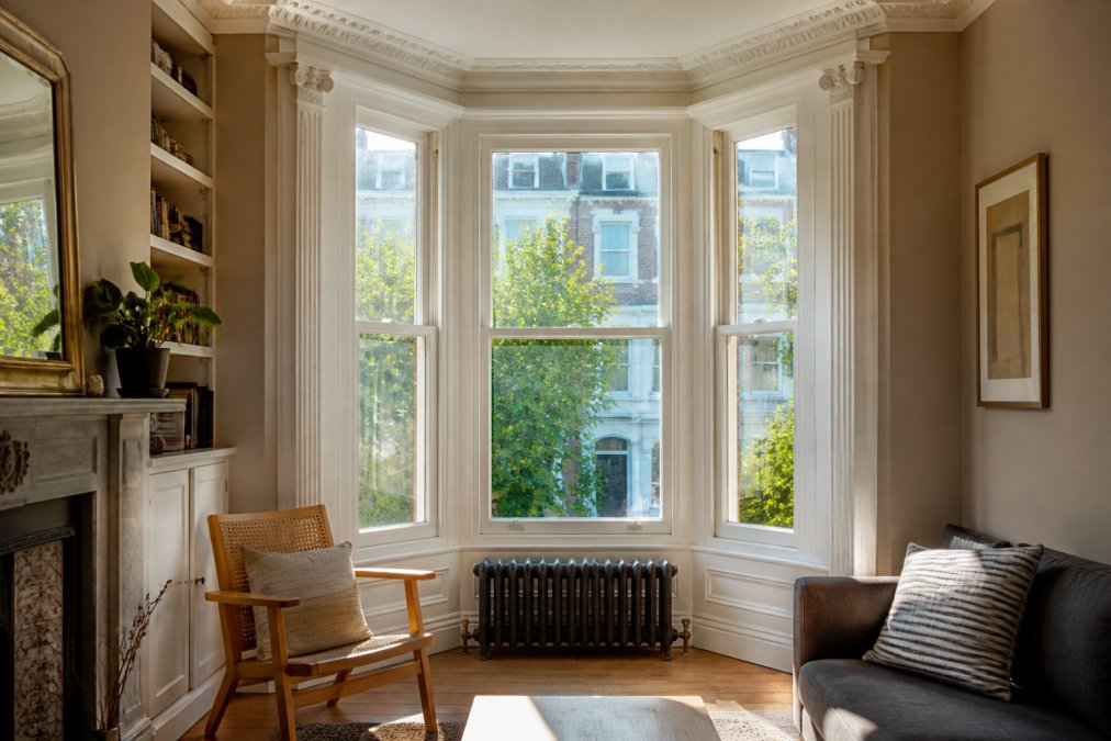 Bright Victorian bay window in a period terrace home showing angled glass panels, architectural detail of the window frame, and natural afternoon sunlight streaming through the glass