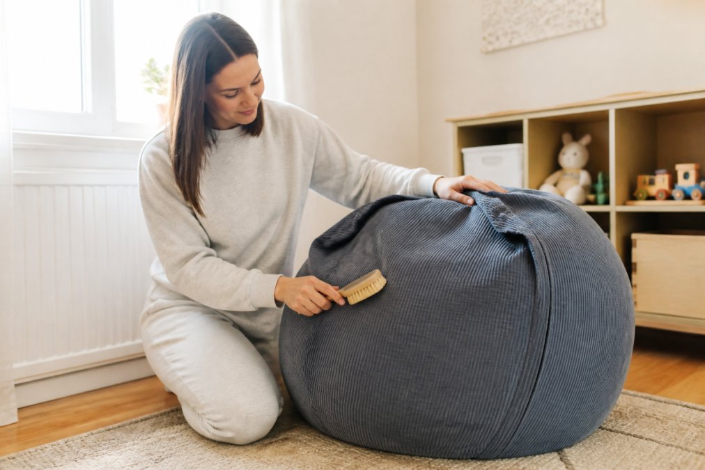 Parent cleaning a child's beanbag cover with a soft brush, gently brushing the washable fabric in a bright home setting with natural light streaming through a window