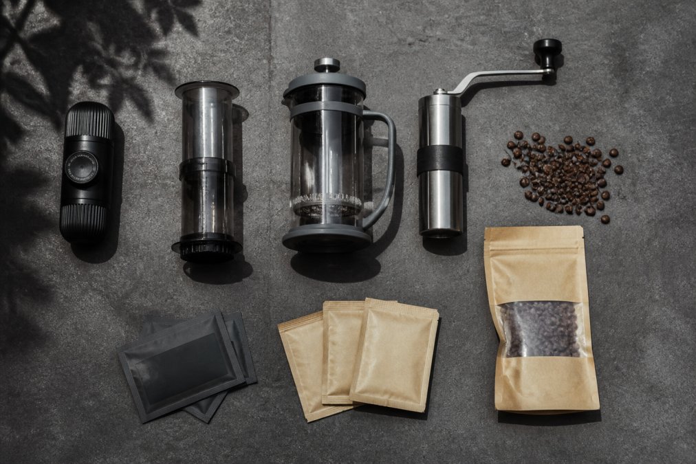 Udstyr til gourmetkaffe til rejsebrug som Nanopresso, AeroPress og kværn arrangeret på en mørkegrå betonplade.