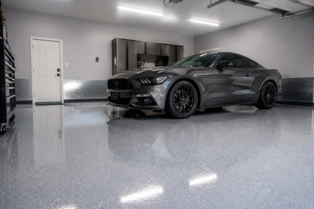 Færdig garage med glinsende epoxy-gulvbelægning, hvor en bil er parkeret på det, og reflekterer overhead-lys, der viser det polerede udseende
