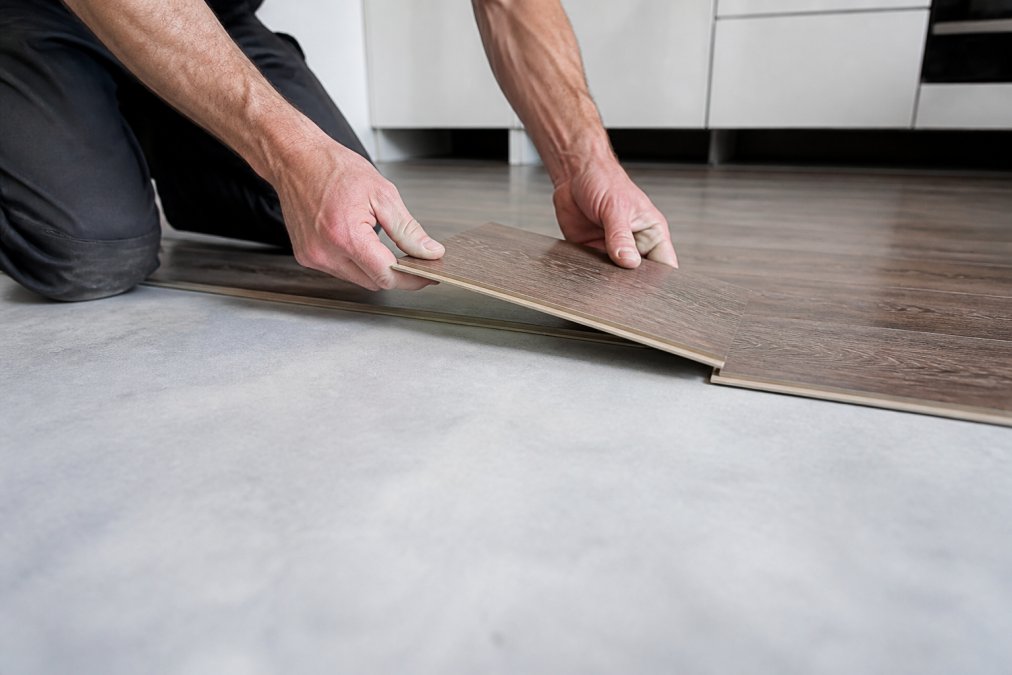 Hænder, der forbinder to vinylplanker med kliksystem i nærbillede, monteringsprocessen vises trin for trin