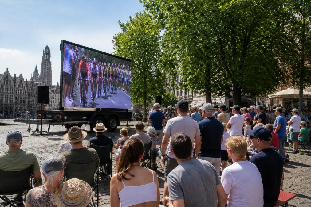 Groot outdoor LED scherm op een evenementenlocatie in de stad, gemonteerd op een aanhangwagen, met bezoekers die vanaf verschillende hoeken naar het scherm kijken tijdens een zomerse dag