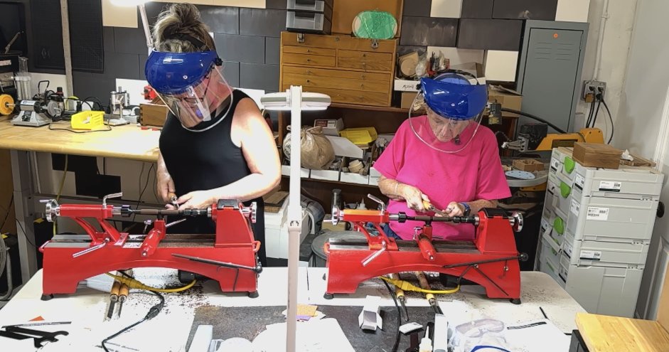 Two students wearing face shields learn pen turning on red wood lathes during a hands-on woodworking workshop at Artists of Elements in St. Petersburg, Florida.